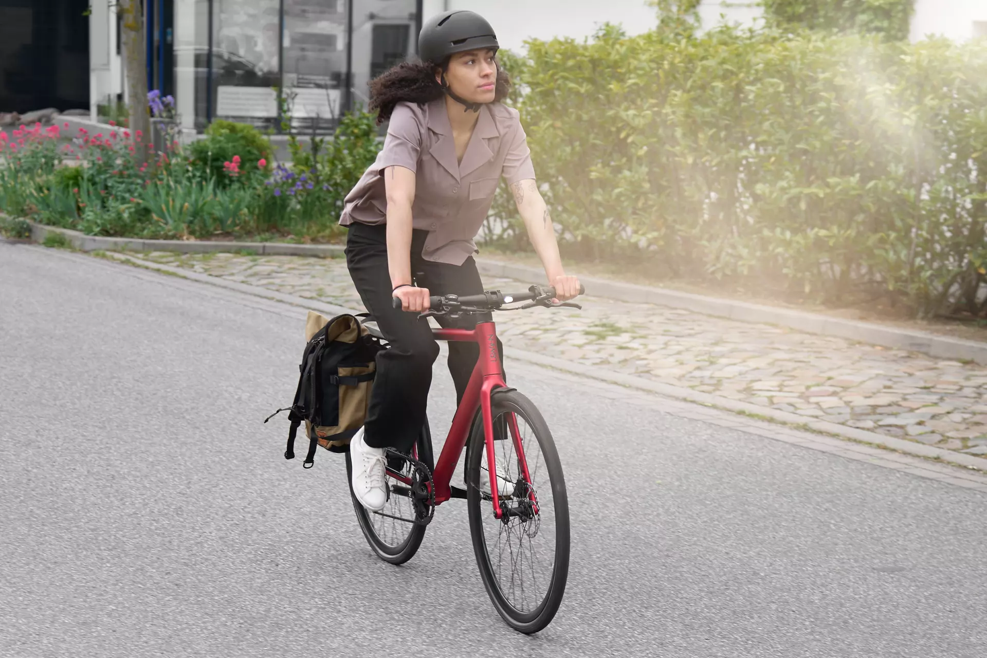 Eine junge modebewusste Frau fährt mit dem roten E-Bike Stadtfuchs inklusive Helm und Radtasche auf der Straße in der Stadt