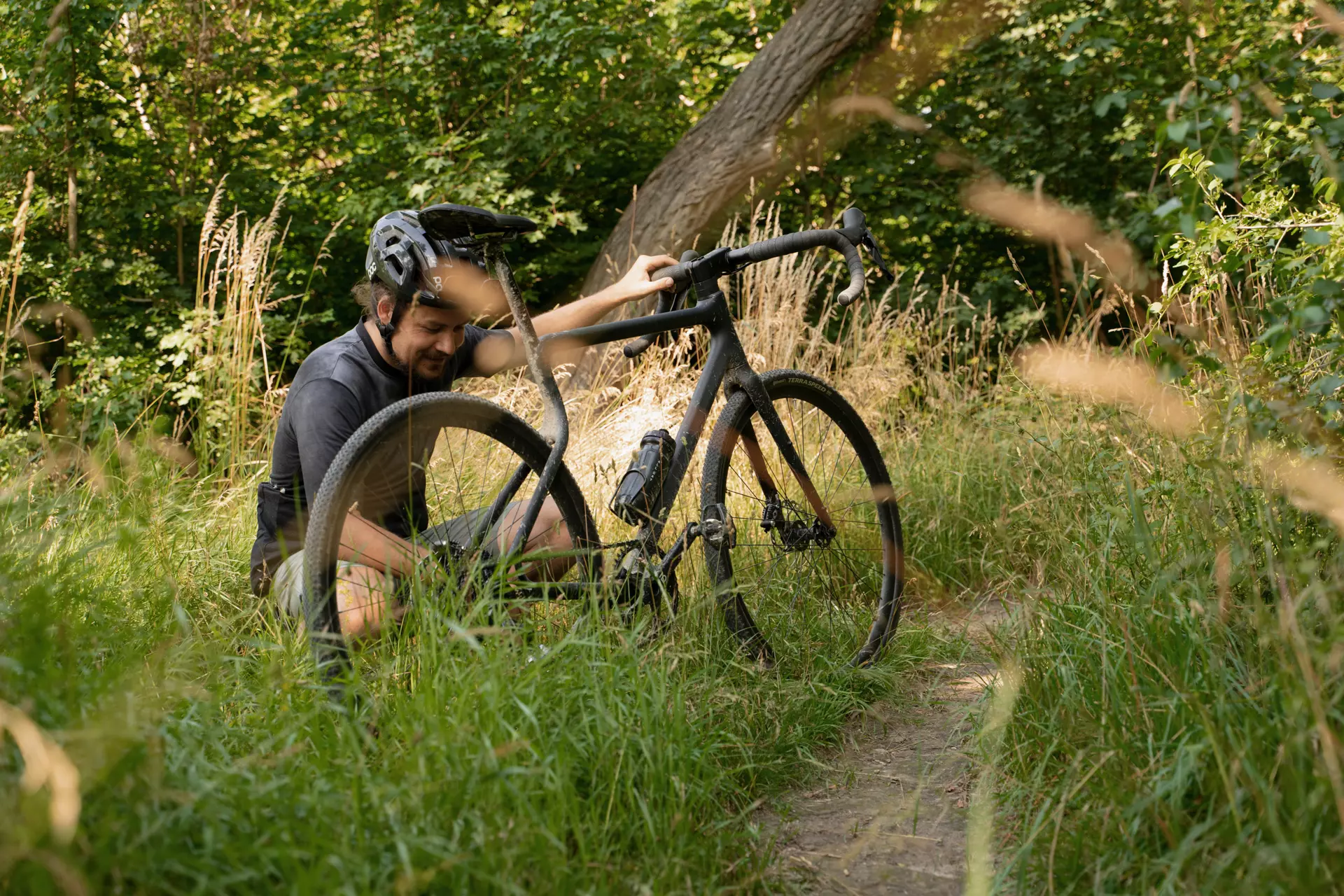 Sportlicher junger Mann pausiert nach einer Graveltour mit dem Gravel Bike Waldwiesel auf einer grünen Wiese am Wegesrand